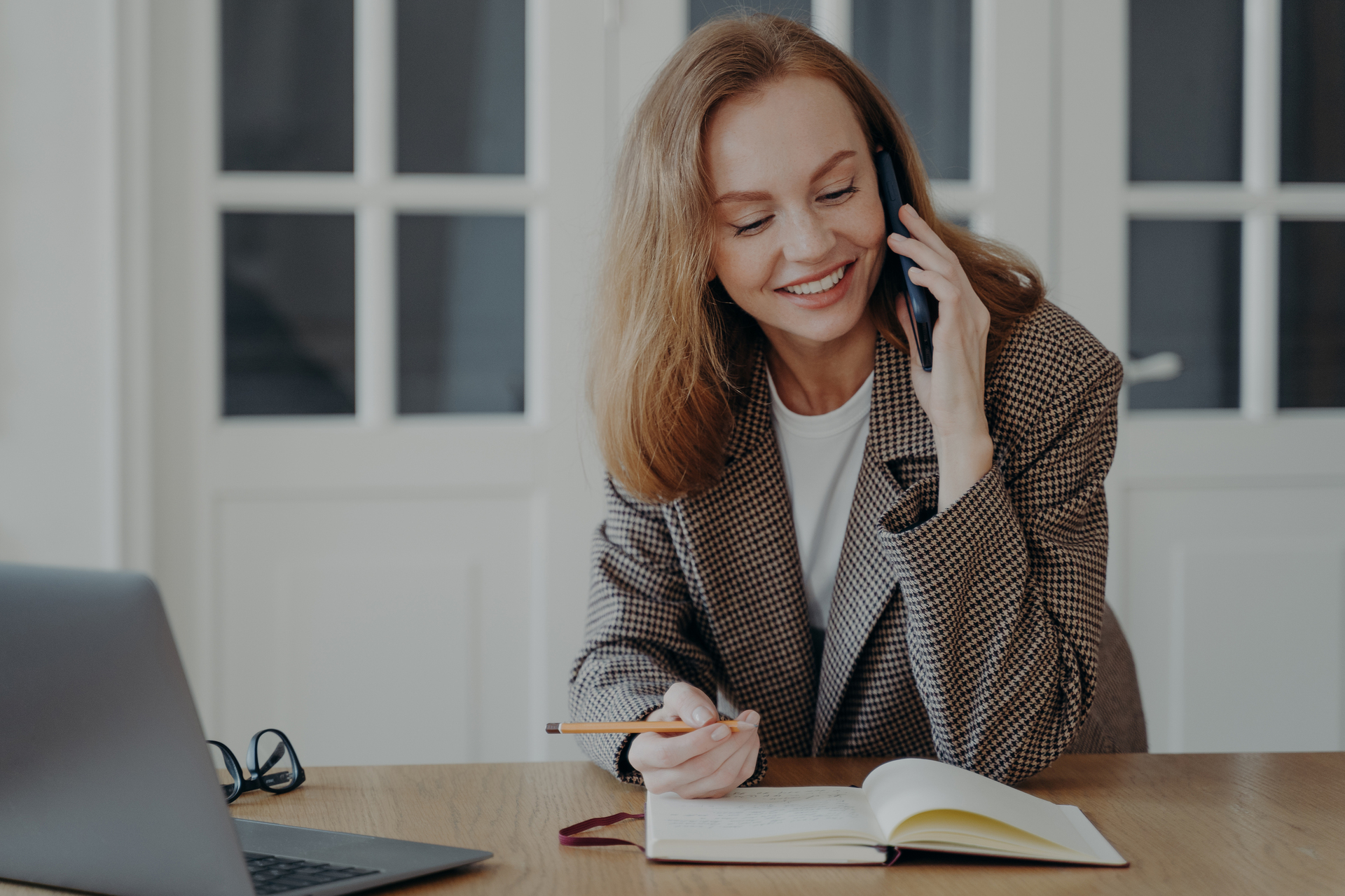 Female employee answers call at desk with laptop, talking on phone, consulting client, making notes